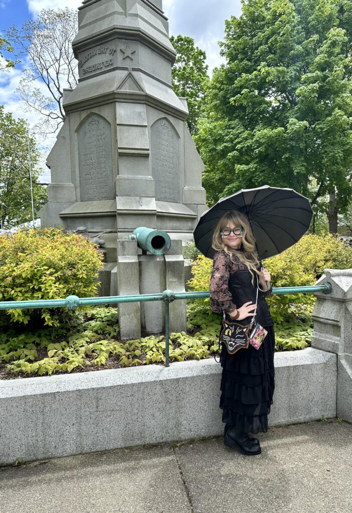 Nikki, wearing a dark outfit with a parasol at a public park