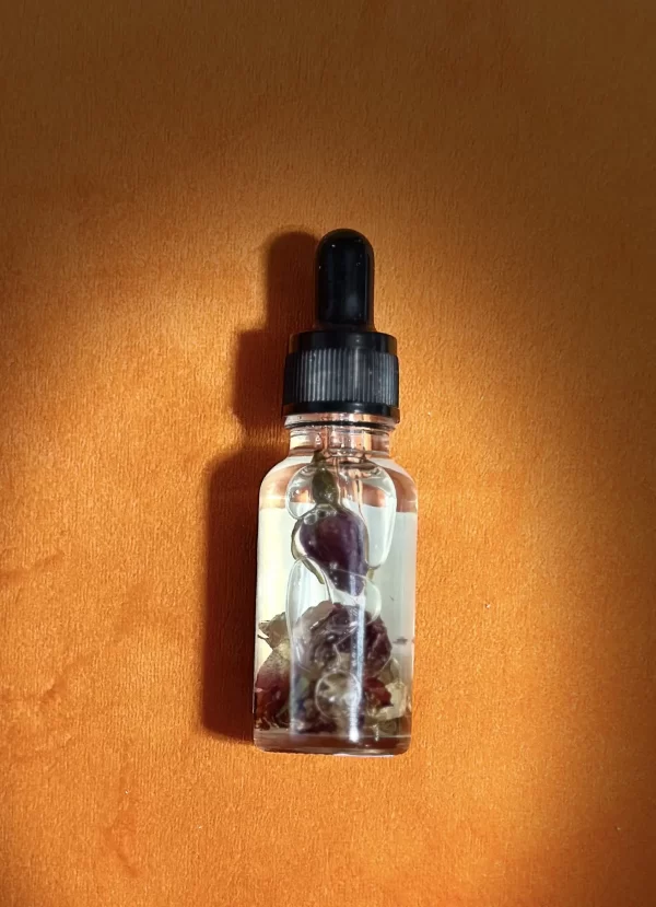 A small, clear glass bottle filled with a liquid containing rose petals. The bottle has a black dropper cap. The background is a soft orange color.