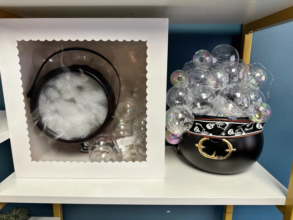 A Halloween crafting kit containing a black cauldron, a white box with faux smoke and bubbles. Next to it is an example completed cauldrom