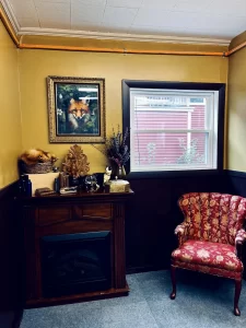 The image shows a cozy corner of the shop, featuring a rustic mantle adorned with mystical decor and natural elements. The fur of a fox, named Mortimer, is draped across the mantle, and above the mantle is a framed picture of Mortimer. The decor around the mantle includes candles, small trinkets, and witchy items, creating a warm and magical atmosphere. The scene evokes a blend of nature, craftsmanship, and enchantment, adding to the shop's unique charm.