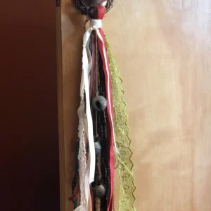 Handmade witch bells hanging on a doorknob, featuring a vine wreath and various colored ribbons with bells attached, used for spiritual cleansing and decoration.