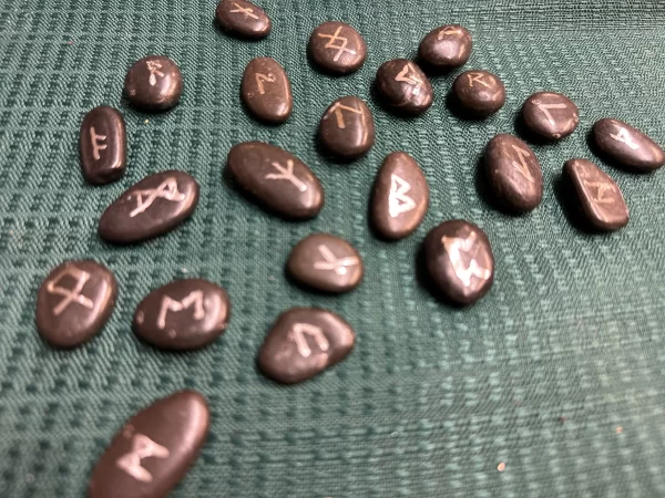 Handmade rune stones displayed on a textured green fabric, featuring various symbols that participants will learn to create in the 'Make Your Own Runes' class.