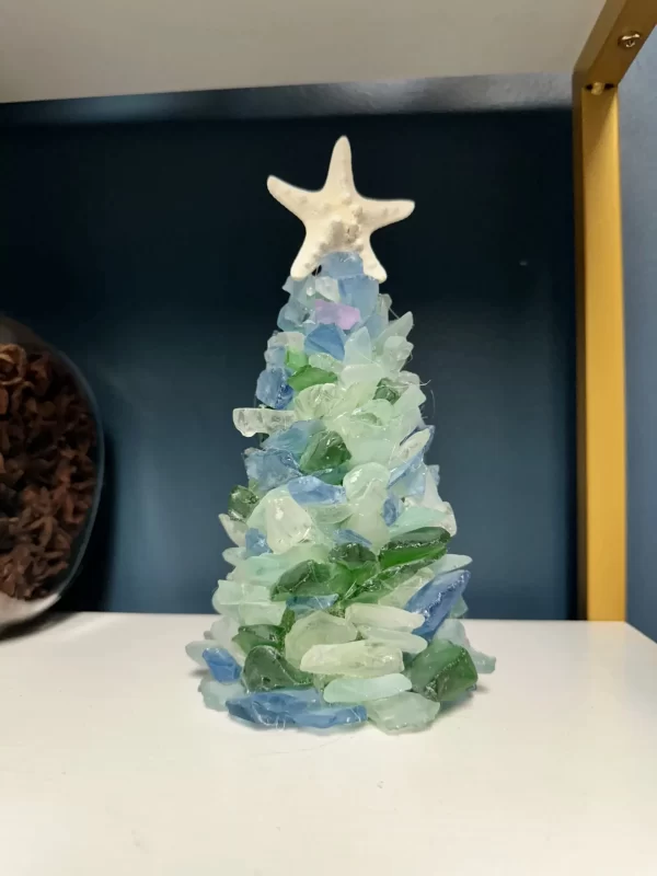 Close-up image of a handmade sea glass Christmas tree, decorated with pieces of blue, green, and clear sea glass, topped with a starfish.