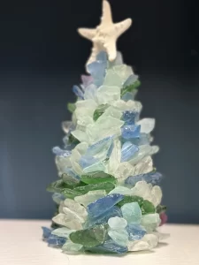 Close-up image of a handmade sea glass Christmas tree, decorated with pieces of blue, green, and clear sea glass, topped with a starfish.