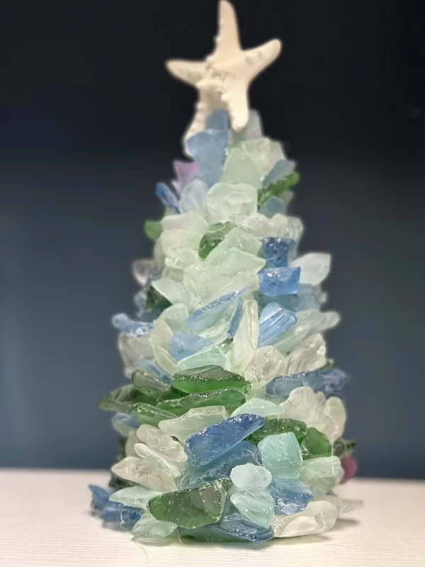 Close-up image of a handmade sea glass Christmas tree, decorated with pieces of blue, green, and clear sea glass, topped with a starfish.