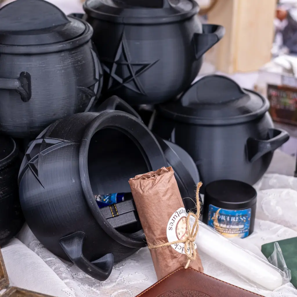 A display of our Beginner Witch Kits ; black 3D-printed Cauldrons with a top that screws into place an containing as selection of items